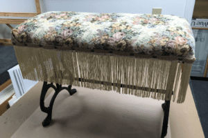Floral upholstered bench with fringe and iron legs