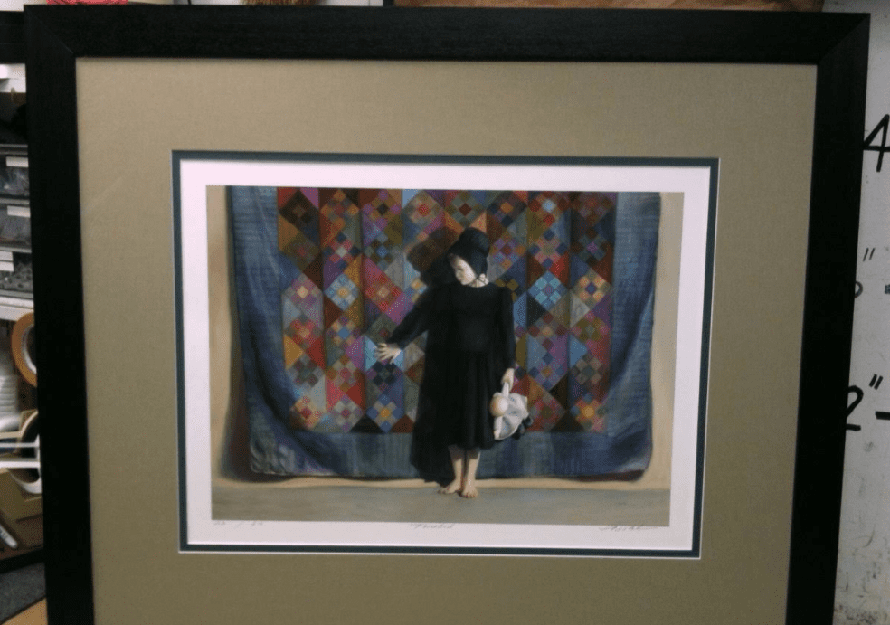 Framed artwork of child with doll, quilt